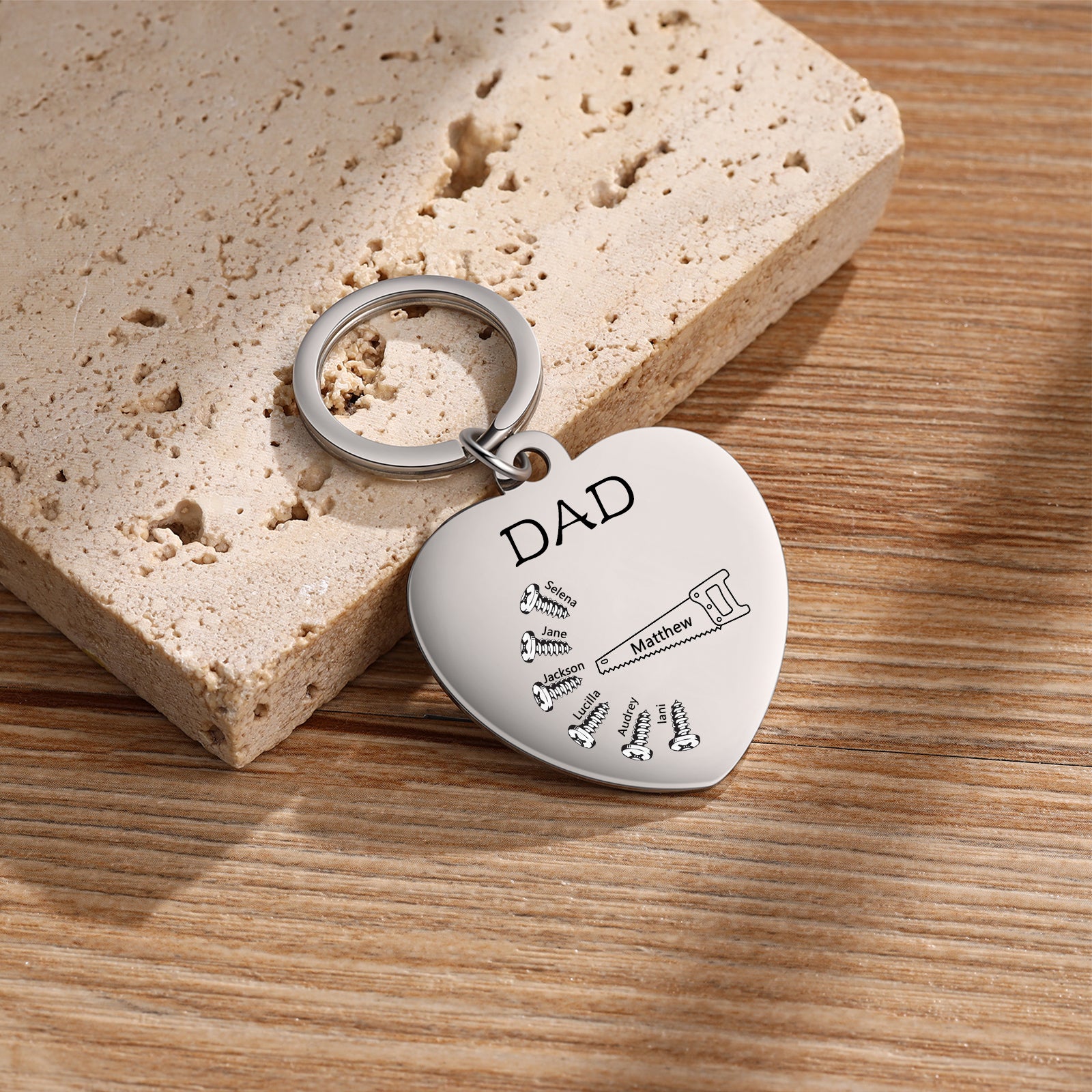 name necklace , Silver heart-shaped keychain with "DAD" inscription and small black key on wood background