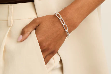 Close-up of a hand wearing a silver bracelet over beige pants, highlighting Bracelets for Women.