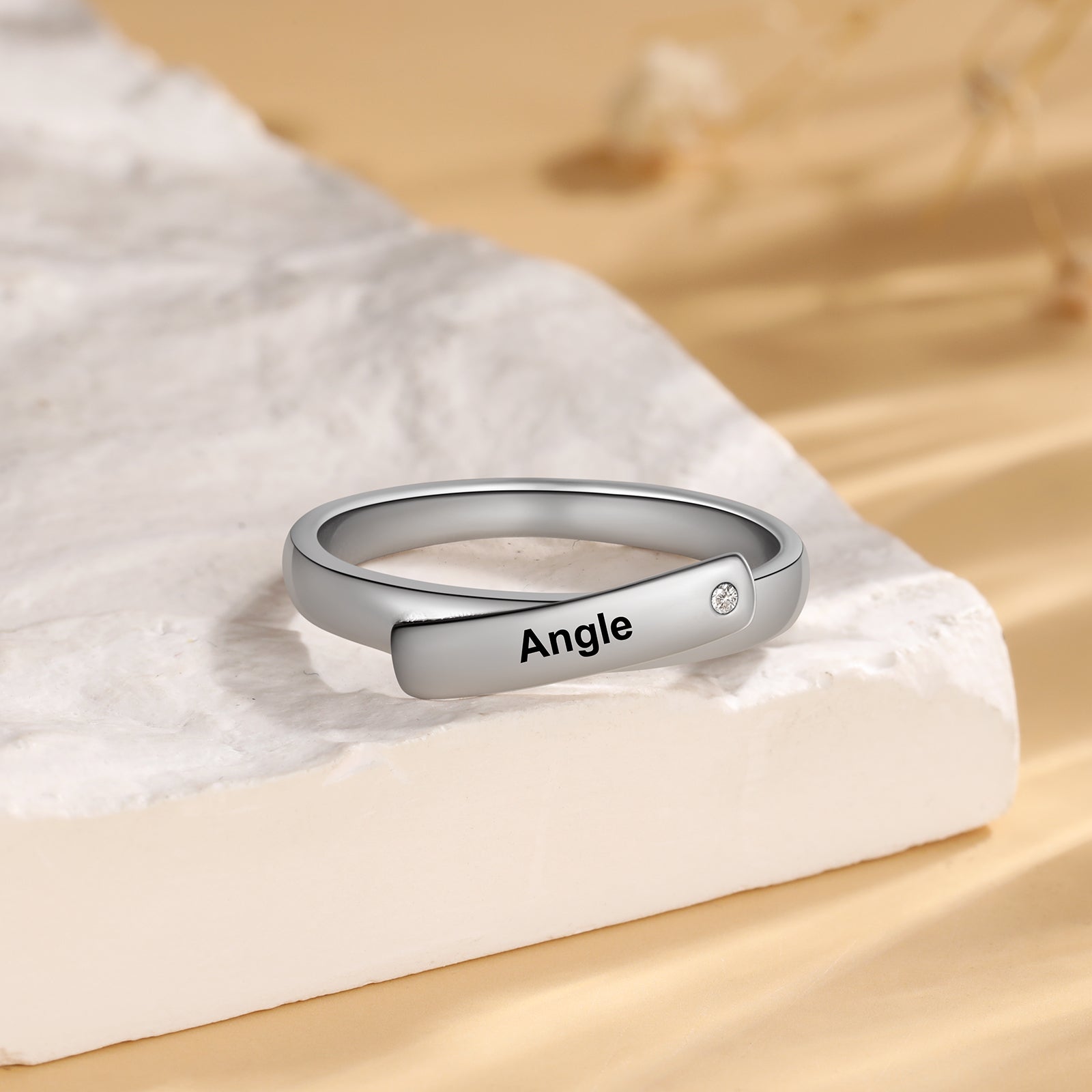 name bracelet, Silver ring with 'Angle' engraving and diamond on white marble surface